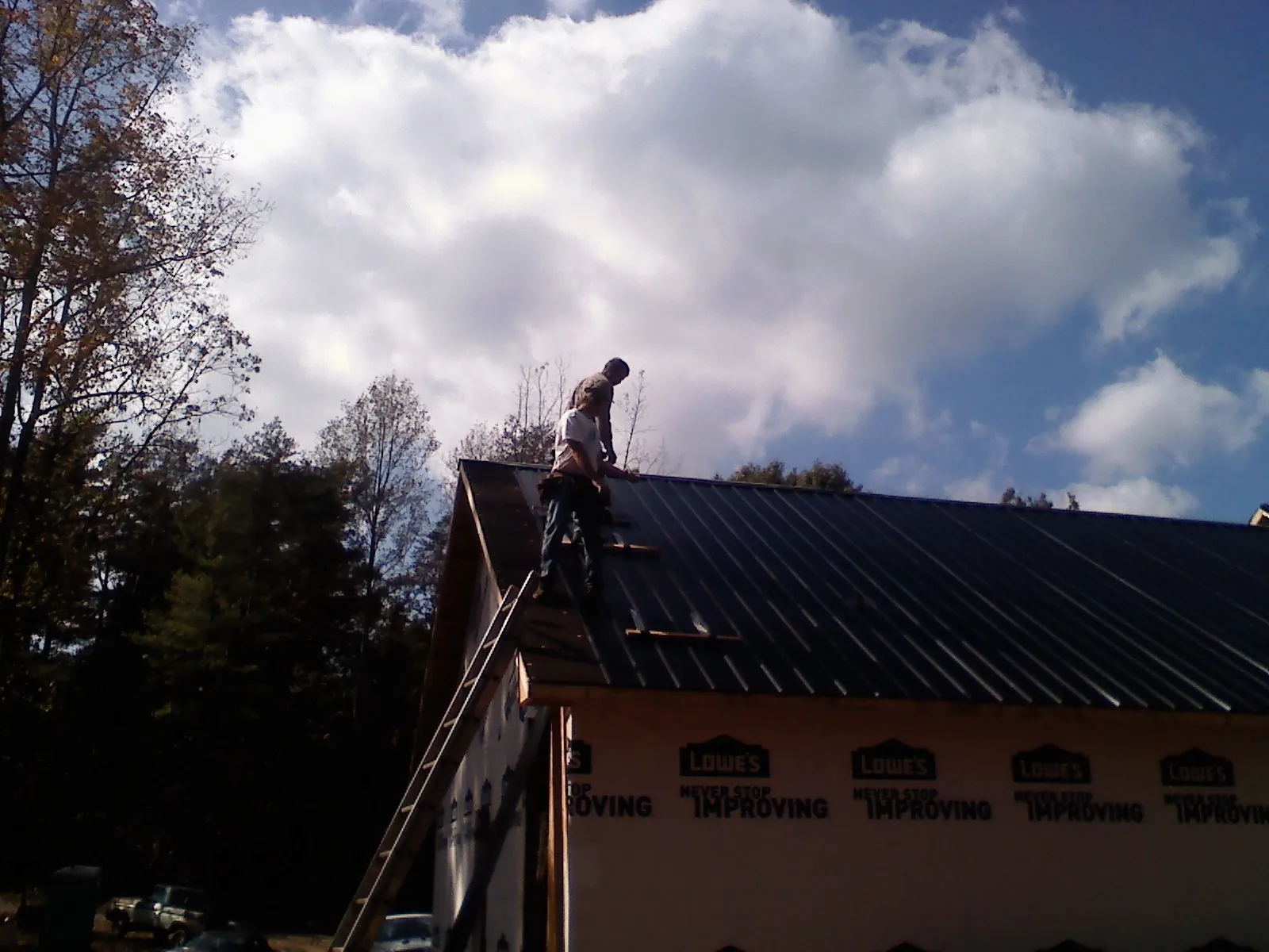 Roofer fastening dark metal panels high against a cloudy sky, from a Roof Inspection job in Palmer